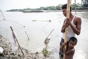 Bangladeshi man and child holding onto bamboo pole in water