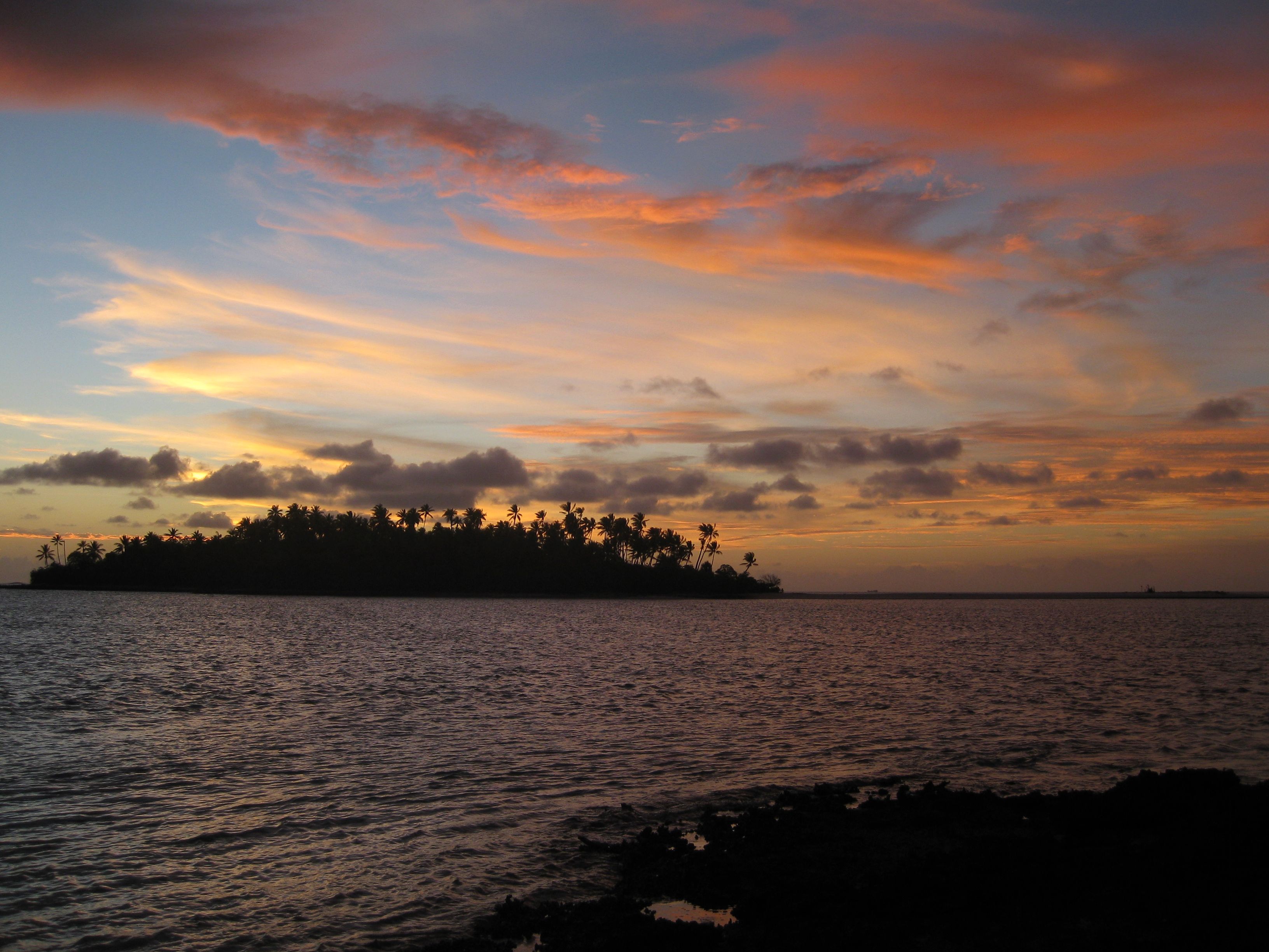 Sunrise over silhouetted Pacific island.