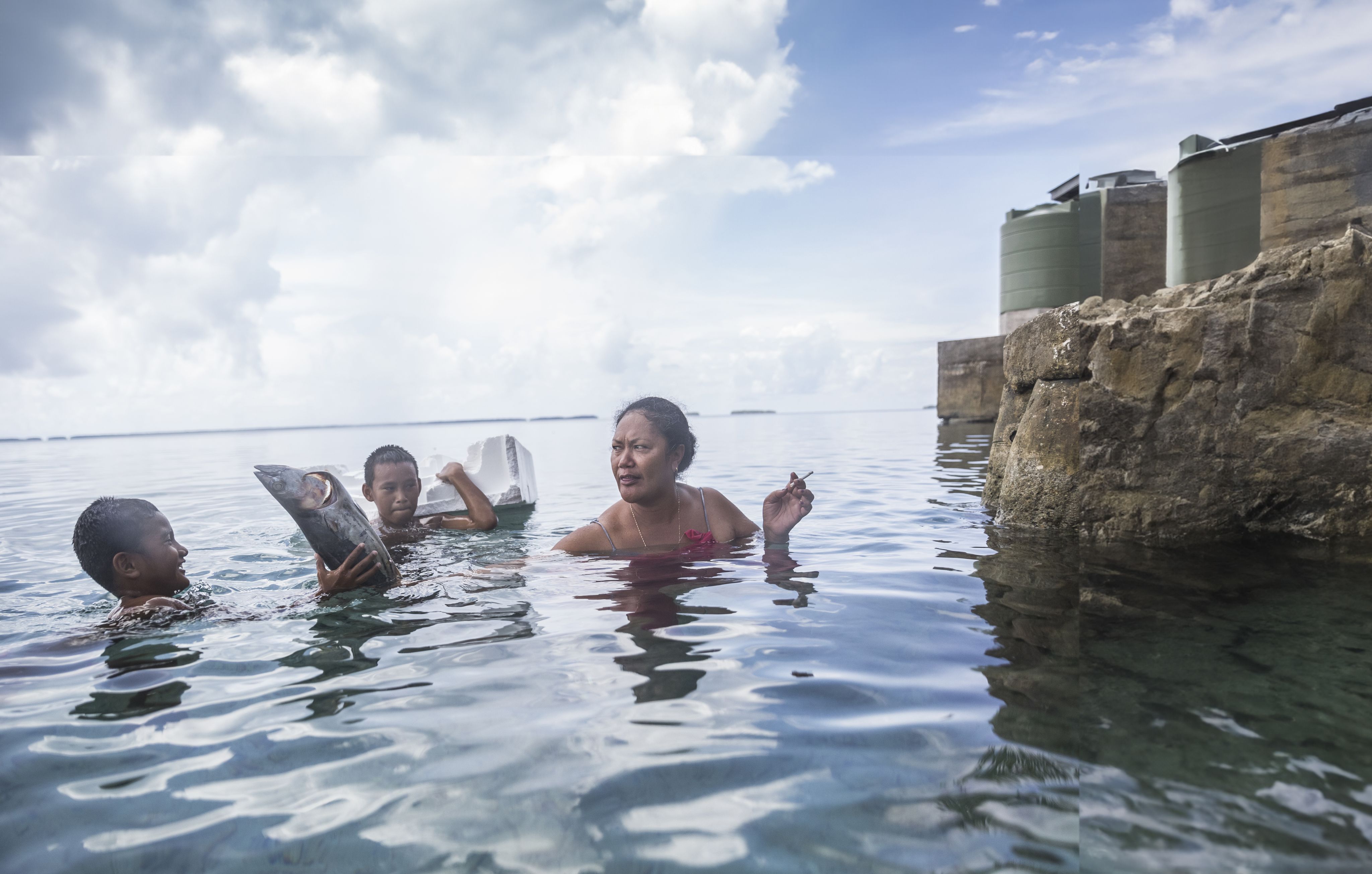 Mother and sons in water with cigarette, fish and debris