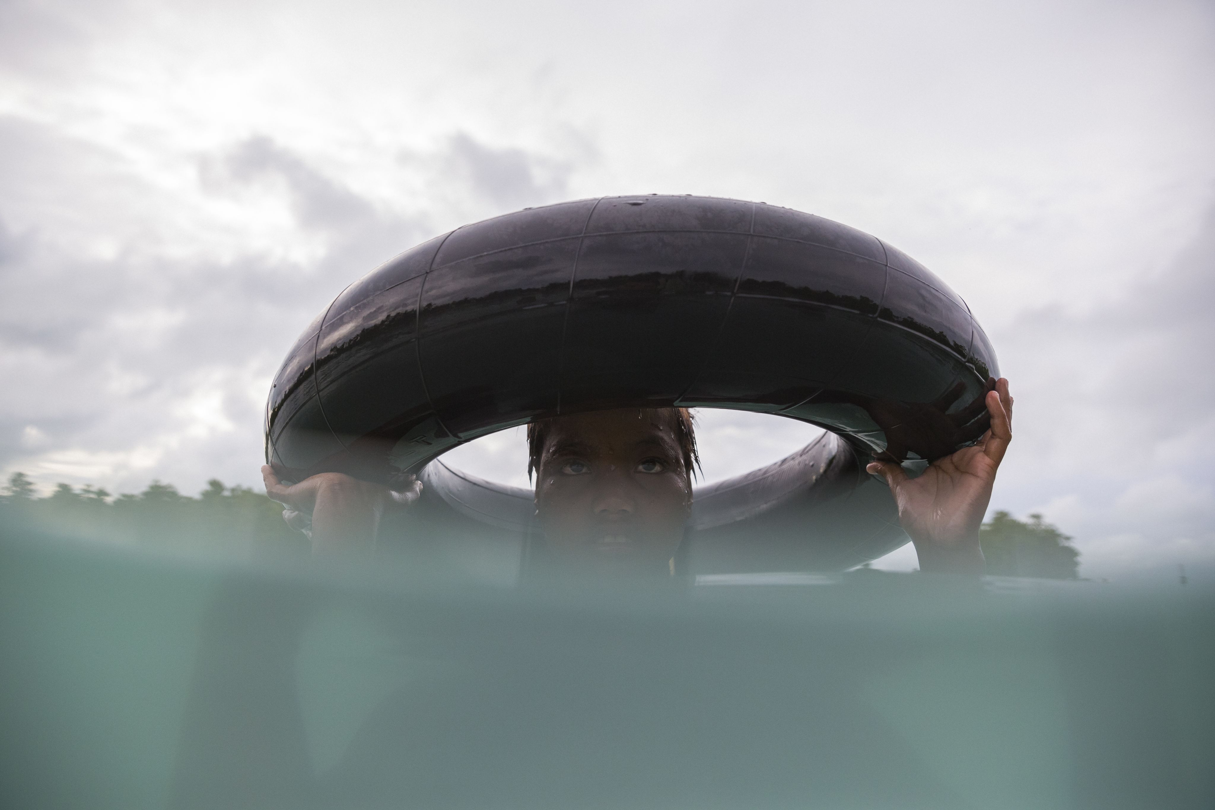 Pacific person in the sea with head above water peeking up through a car tire.